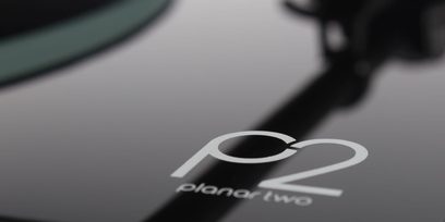 Nærbillede af "P2"-logoet, der er indgraveret i den sorte lakerede plade på en Rega Planar 2 hi-fi pladespiller, set ovenfra