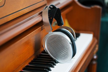 Primer plano de unos auriculares circumaurales plateados de metal con cáscaras perforadas, colocados sobre las teclas de un piano vertical de madera