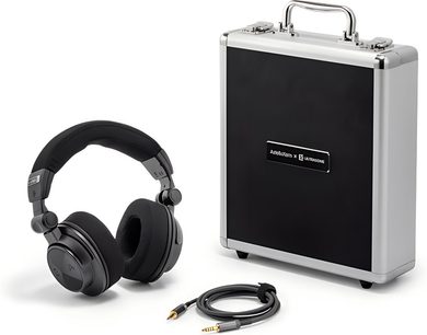 Třičtvrtinový pohled zepředu na uzavřené hi-fi sluchátka Astell&Kern Virtuoso v černé matné plastové barvě s polstrovaným náhlavním páskem a polstrovanými náušníky, doplněné o odnímatelný černý kabel s pozlaceným jack konektorem a pevným hliníkovým pouzdrem v šedé barvě s černým panelem.