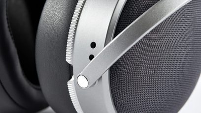 Close-up side view of the earcup of the closed-back wired Audeze LCD-S20 hi-fi headphones in silver metal, featuring a notched crown, dark gray mesh fabric outer shell, and a large black faux leather earpad