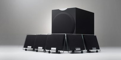 Seks kompakte sorte Waterfall Audio Pack 1 højttalere på stativer, opstillet i en halvcirkel, med kubiske basenheder