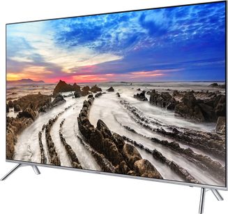 Samsung UE55TU7005-TV som visar en flygvy över en stenig strand vid solnedgången med en färggrann molnig himmel