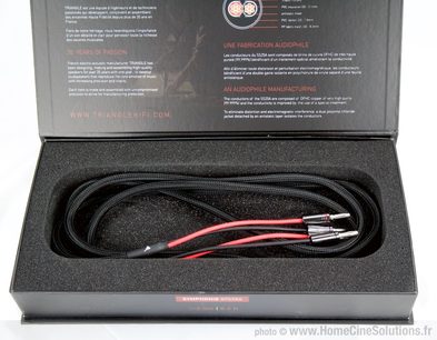 Sort lydkabel med røde stik, oprullet i en rektangulær sort boks, liggende på en grå brochure