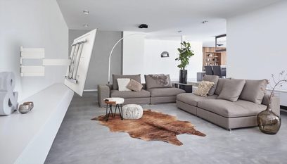 Sala de estar moderna com sofá de canto cinzento, almofadas decorativas, tapete de pele de vaca, mesas de centro redondas, prateleira de parede e planta verde