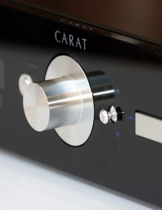 Børstet metalrotationsknap på blankt sort panel, med indskrifterne "CARAT" og strømsymbol, tæt forfra-udsigt
