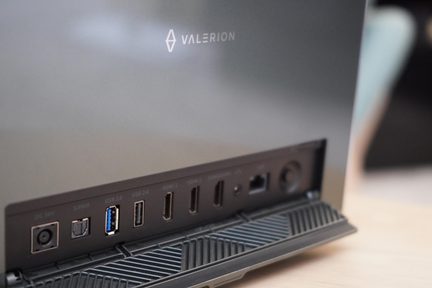 Nära bild i sned vinkel på baksidan av en apparat i matt antracitgrå metall och plast, försedda med den vita logotypen "VALERION", en rad uppställda portar (ström, optiskt ljud, blå USB 3.0, USB 2.0, två videoportar, Ethernet) och ett svart rillat stöd.