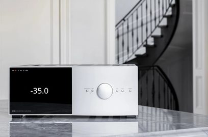 Anthem STR entegre gümüş hi-fi stereo amplifikatör, önden görünüm, ekranda "-35.0" gösteriliyor, yansıtıcı bir yüzey üzerine yerleştirilmiş, arka planda merdivenler