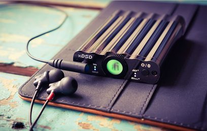 Bærbar iFi Audio xDSD sort lydkonverter, set ovenfra, med knapper og stik på siden, liggende på en brun lædertaske