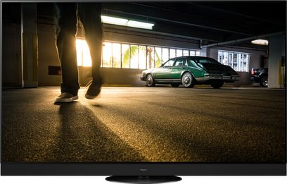 Téléviseur Panasonic TX-65MZ1500E vert garé dans un garage sombre, vu de face, avec une personne en arrière-plan