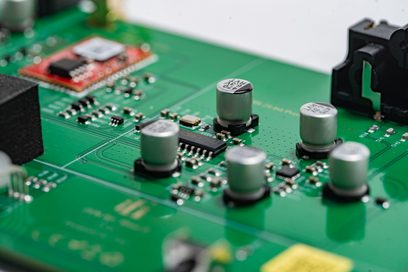 Detailní záběr na zelenou elektronickou desku se stříbrnými kondenzátory a černými mikrokomponenty
