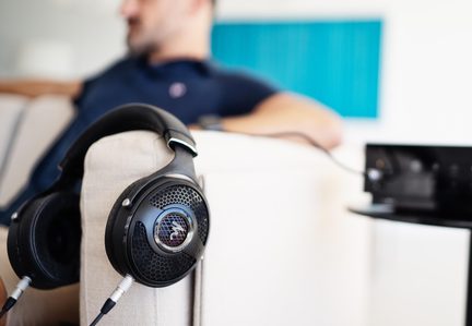 Zwarte circumaurale koptelefoon van leer en metaal, oorschelp met honingraatgrill, close-up zijaanzicht hangend aan de beige armleuning van een bank