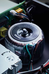 Set ovenfra af en Magnat toroidal transformer med farvede kabler tilsluttet og teksten "To reduce the risk of electric shock"