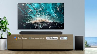TCL-fladskærm, der viser et turkisfarvet undervandsscene, placeret på et lyst trækabinet med den integrerede soundbar TS8132