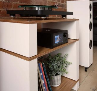 NAD C700 V2 fekete sztereó hi-fi erősítő fa polcon, bekapcsolt képernyővel, lemezjátszó a tetején, fehér hangszóró jobboldalt