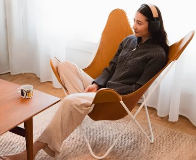 Fones de ouvido sem fio pretos e bege usados por uma mulher sentada em uma poltrona lounge laranja