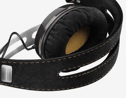 Sort hovedtelefon med beige stofpuder, polstret hovedbøjle og flettet kabel, set fra en trekvart bagfra vinkel