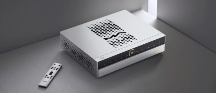 Rektangulært elektronikhus i lysegrå aluminium, set i trekvart vinkel forfra, sort blank front med centralt cirkulært display “68” og justerbare touch-knapper på linje, top med cirkulære perforeringer i zigzagmønster, siderne også perforerede, flad sølvfarvet fjernbetjening placeret ved siden af