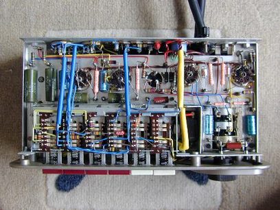 Widok wnętrza otwartego wzmacniacza audio Quad II + Quad 22, ukazujący kolorowe komponenty elektroniczne i kable na metalowej ramie