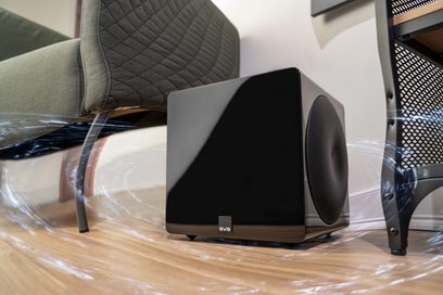 SVS 3000 Micro negru lucios subwoofer, vedere frontală, pe un parchet, cu un fotoliu în fundal