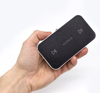 Sort Octavio Stream netværksaudioafspiller, holdt i en hånd, set forfra og fra siden, med logo og knapper synlige