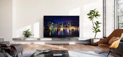 Téléviseur affichant une ville illuminée la nuit, posé sur un meuble dans un salon moderne avec un fauteuil et une plante