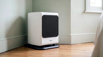 Valkoinen Canton-subwoofer mustalla etupaneelilla, lattialle asetettuna seinän viereen modernissa sisustuksessa