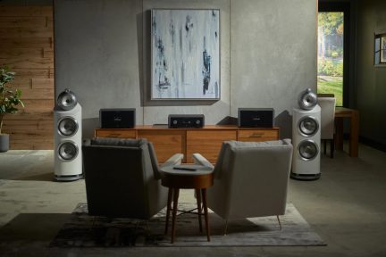 Două fotolii gri în fața unui mobilier din lemn cu trei aparate audio negre, două boxe albe, tablou abstract