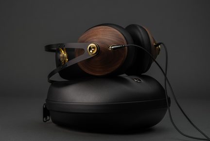 Casque audio, coques en bois brun, arceau métal noir et accents dorés, câble à fiche, vue latérale, sur étui rigide noir