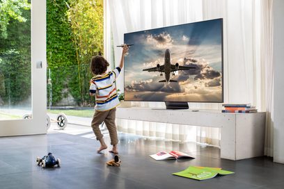 Televizor Samsung QE55Q95T 2020 zobrazující letadlo na pozadí oblačné oblohy před dítětem, které ukazuje na obrazovku
