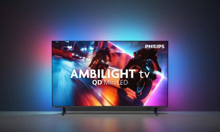 Sort, fladskærms-tv med tynd metalramme, set forfra, stående på to sorte fødder, med dynamisk display og flerfarvet Ambilight-lysglød omkring skærmen