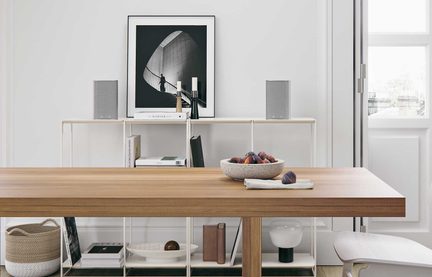 Gray wireless speakers on a white shelf, Scandinavian decor with a black-and-white photo and a light wood table