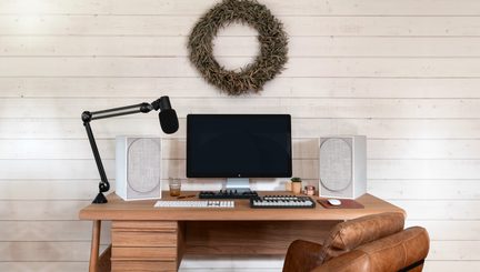 Wooden desk with computer, keyboard, mouse, speakers, microphone, and a wreath of leaves on the wall