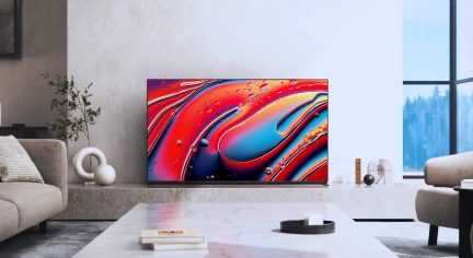 Moderne stue med beige sofa, marmorbord, fladskærms-tv, der viser abstrakt kunst, vindue med udsigt til skov