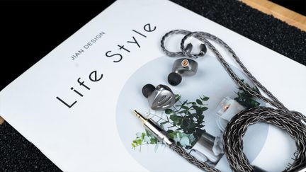 Gråmetallic ledningsforbundne in-ear høretelefoner i aluminium med sorte silikonepropper, antracitgrå flettet kabel og 3,5 mm jackstik, set fra oven