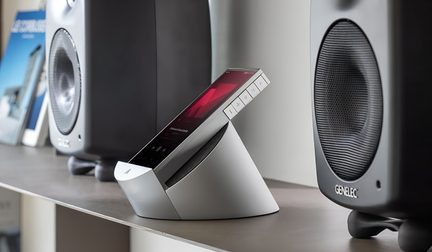Srebrne metalowe urządzenie audio z stożkową podstawą, pochylony czarny ekran dotykowy z pięcioma bocznymi przyciskami, widok z lewego przedniego kąta