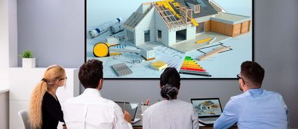 Billedet viser fire personer, der sidder foran en stor skærm, der viser en 3D-model af et hus med byggetegninger og værktøjer
