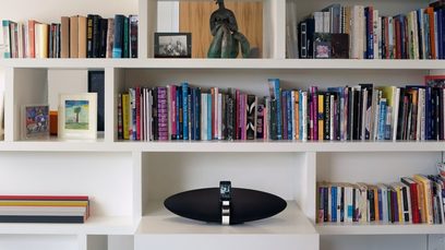 Must Bowers & Wilkins Zeppelin Air õhukõlar tseppelini kujuga valge riiuli peal raamatukoguga taustal