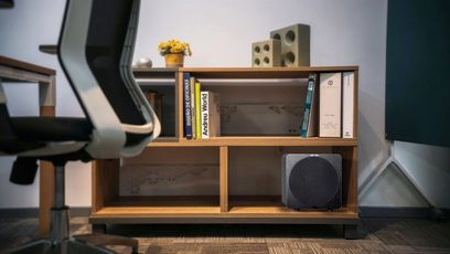 Velodyne Deep Blue 8 sort subwoofer, træhylde, bøger, potteplante, grå kontorstol, parketgulv