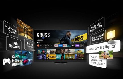 Televisor negro de pantalla plana grande de vidrio y plástico, vista frontal, mostrando una interfaz de streaming colorida, rodeado de burbujas de texto que nombran calidad Hollywood, grabación USB, sintonizador penta, modo juego extremo, Apple AirPlay y controles por voz Alexa, con una pequeña lámpara conectada iluminada a la derecha