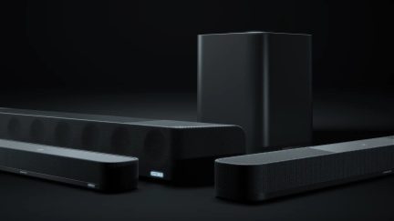 Barre sonore rettangolari nere con griglie a rete, angoli arrotondati, logo visibile, subwoofer nero sullo sfondo