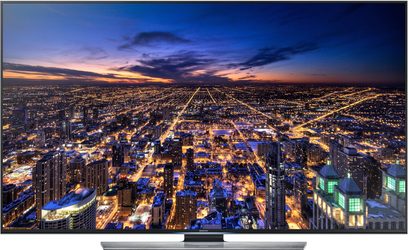 Samsung UE48HU7500 TV viser et natteluftsyn over en oplyst by med tætpakkede bygninger og gittermønstrede gader