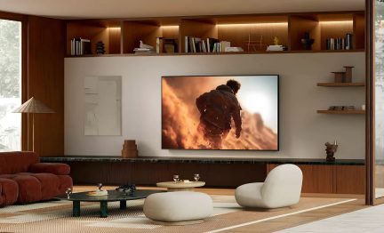 Gran televisor de pantalla plana fijado a la pared en un salón moderno con biblioteca de madera y sillones blancos