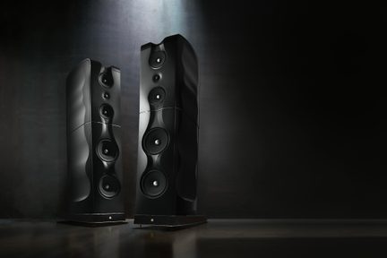 Sæt sorte hi-fi gulvhøjttalere med bølget design og flere højttalerenheder, set forfra mod mørk baggrund