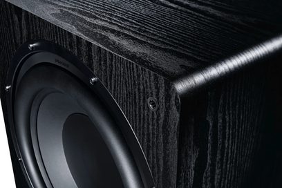 Sort Alpha RS 8 subwoofer med trætekstureret overflade, set fra en vinkel, der viser en cirkulær højttaler og en metalindsats