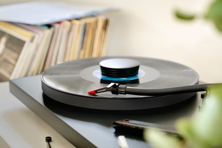 Črn gramofon s črno ploščo, ročica z rdečo iglo, rahlo poševni bližnji posnetek