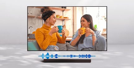 Svart platt-TV med tunn ram i metall och plast, sedd framifrån, med en rektangulär svart soundbar under skärmen, som visar två personer som samtalar i en inomhusmiljö.