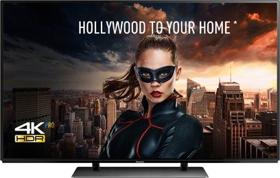 Panasonic TX-65EZ950E 65" 4K HDR-tv der viser en maskeret kvinde foran et bymiljø i solnedgang