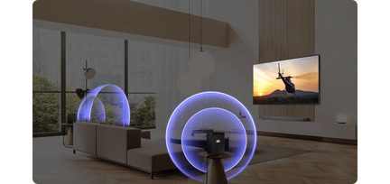Schrägansicht eines modernen Wohnzimmers mit einem schwarzen, rahmenlosen Wandfernseher, einer silbergrauen Soundbar unter dem Bildschirm und zwei schwarzen, würfelförmigen Audioeinheiten aus Kunststoff, die von blauen Lichtkreisen umgeben sind und die Schallausbreitung veranschaulichen.