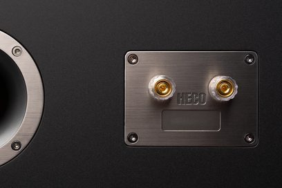 Heco AURORA XT Center 30 centerhøjttaler, delvis bagudvendt visning, rektangulær metalplade med 2 forgyldte terminaler og 4 sølvfarvede skruer