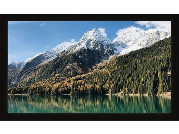 Munți înzăpeziți și o pădure de conifere se reflectă într-un lac liniștit sub un cer albastru cu câțiva nori